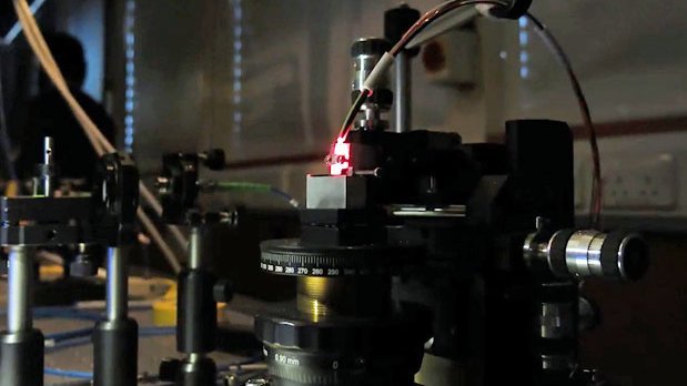 Symbolbild: Nahaufnahme Einkoppelung von Laserlicht in einen optischen Mikrochip über ein herkömmliches Glasfaserkabel
