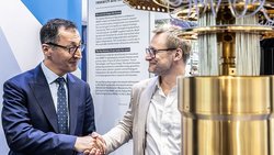 Cem Özdemir schüttelt Markus Bendele die Hand, daneben ein Kryostat eines Quntencomputers
