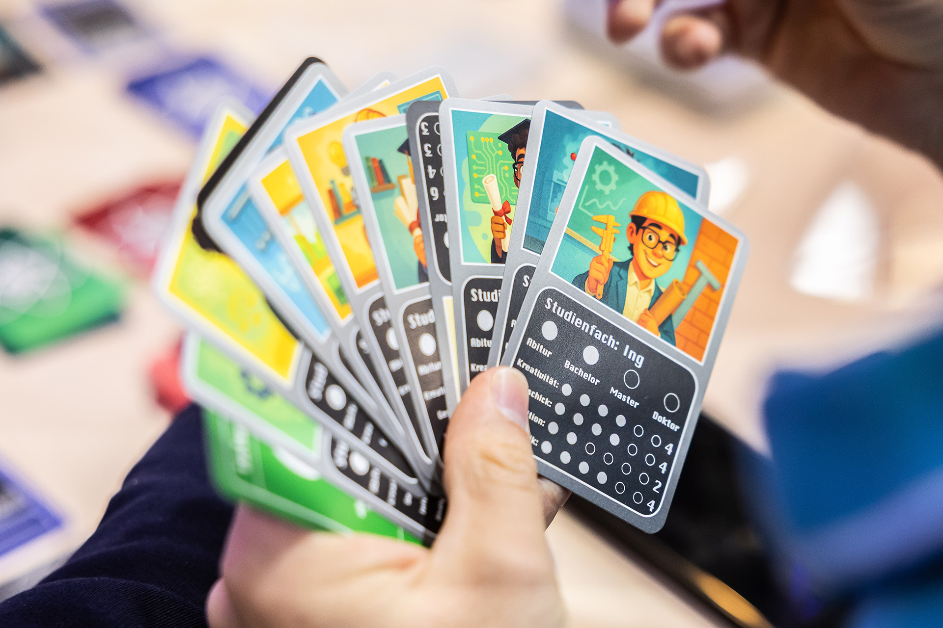 Eine Hand hält bunte Spielkarten. Auf den Karten sind verschiedene Comicfiguren zu sehen, die Forschende aus dem Bereich Quantentechnologien symbolisieren.
